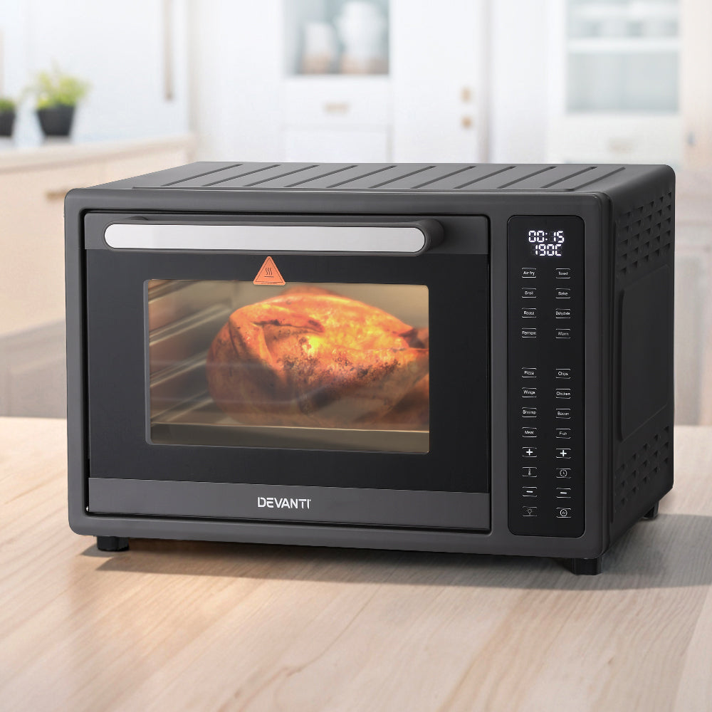 Black Devanti toaster oven with a pizza inside on a wooden surface.