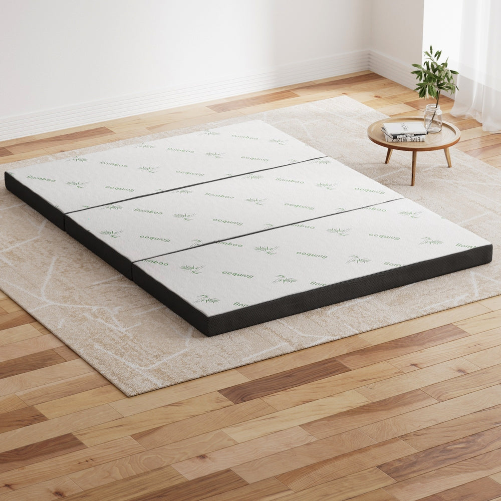Mattress on a wooden floor with a small table and plant in the background