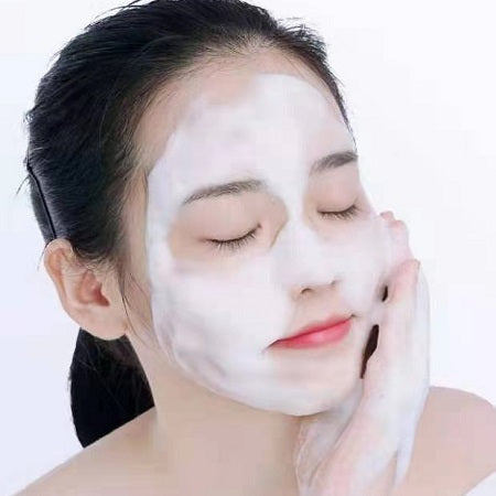 Woman applying a white facial mask on a plain background