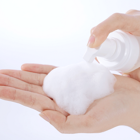 Hand holding a bottle of white foam against a white background