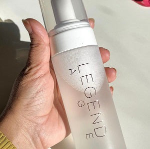 Hand holding a Legend skincare bottle against a blurred background