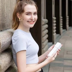 Woman holding a white bottle outdoors on a stone pathway