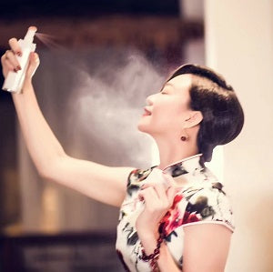 Woman in a floral dress spraying a product, with a blurred background