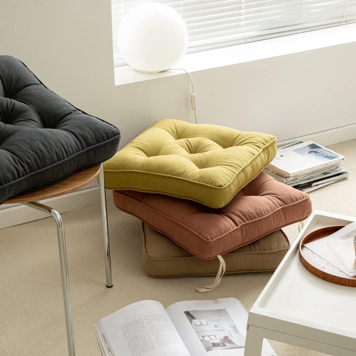 Stack of colorful cushions on a chair in a room with a window and books.