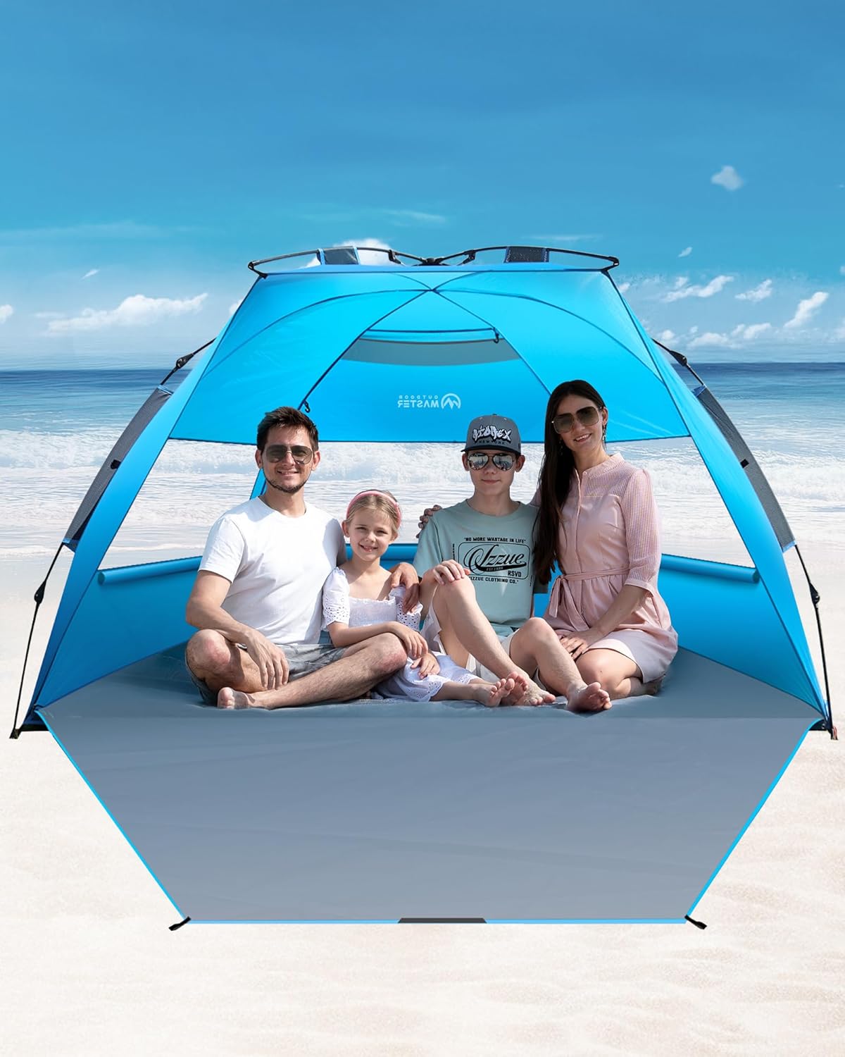 Family sitting under a blue beach tent on a sandy beach with ocean view