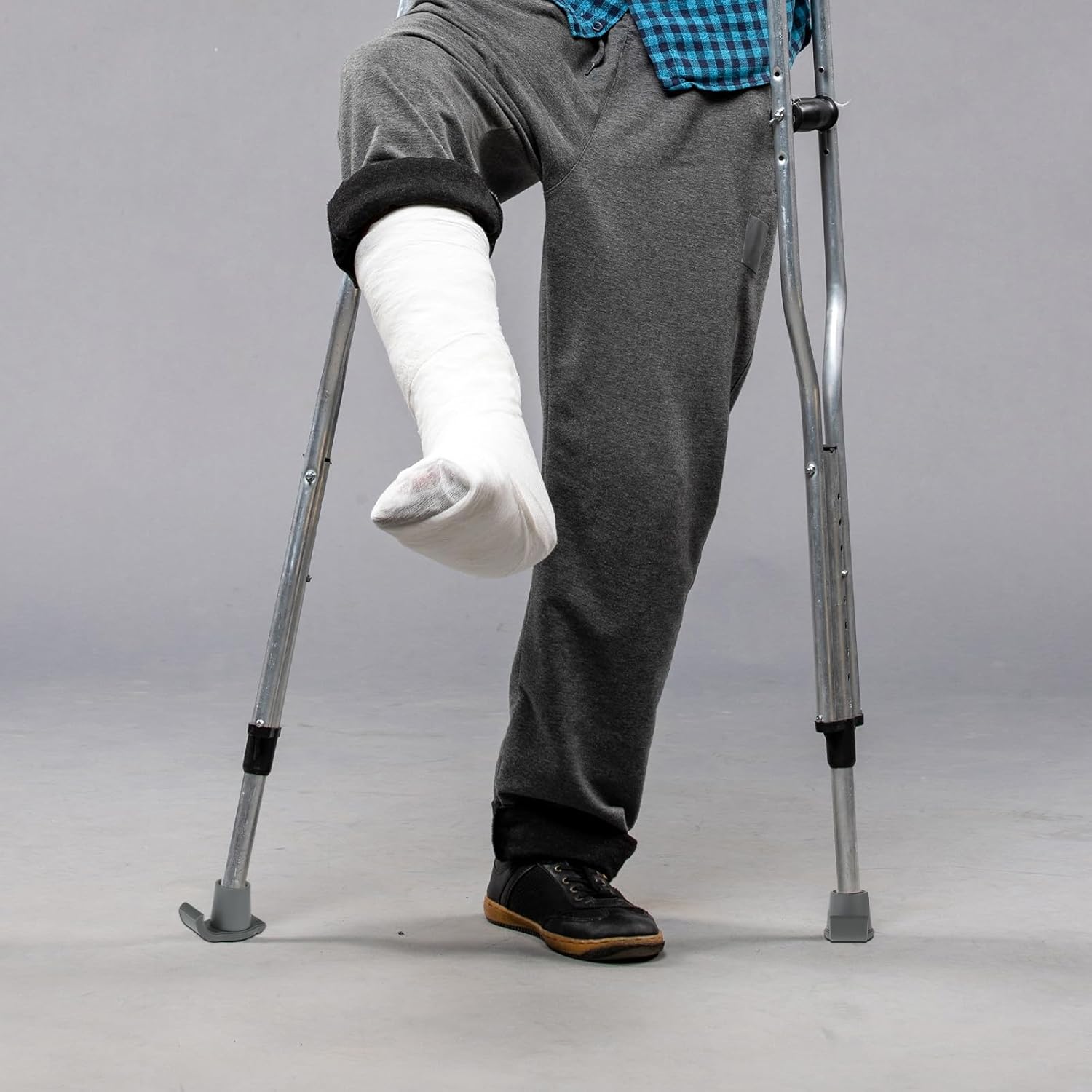 Person using crutches with a casted foot on a plain background