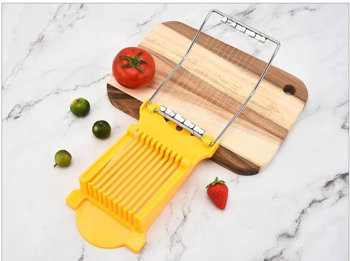 Yellow mandoline slicer on a wooden cutting board with vegetables on a marble surface
