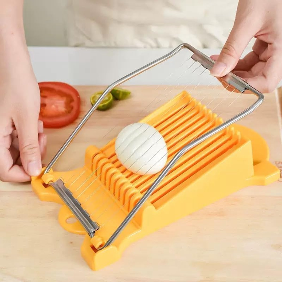 Yellow vegetable slicer cutting an onion on a wooden cutting board with a tomato and green pepper in the background.