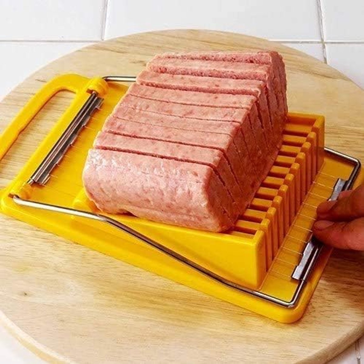 Yellow meat slicer cutting a block of meat on a wooden board.