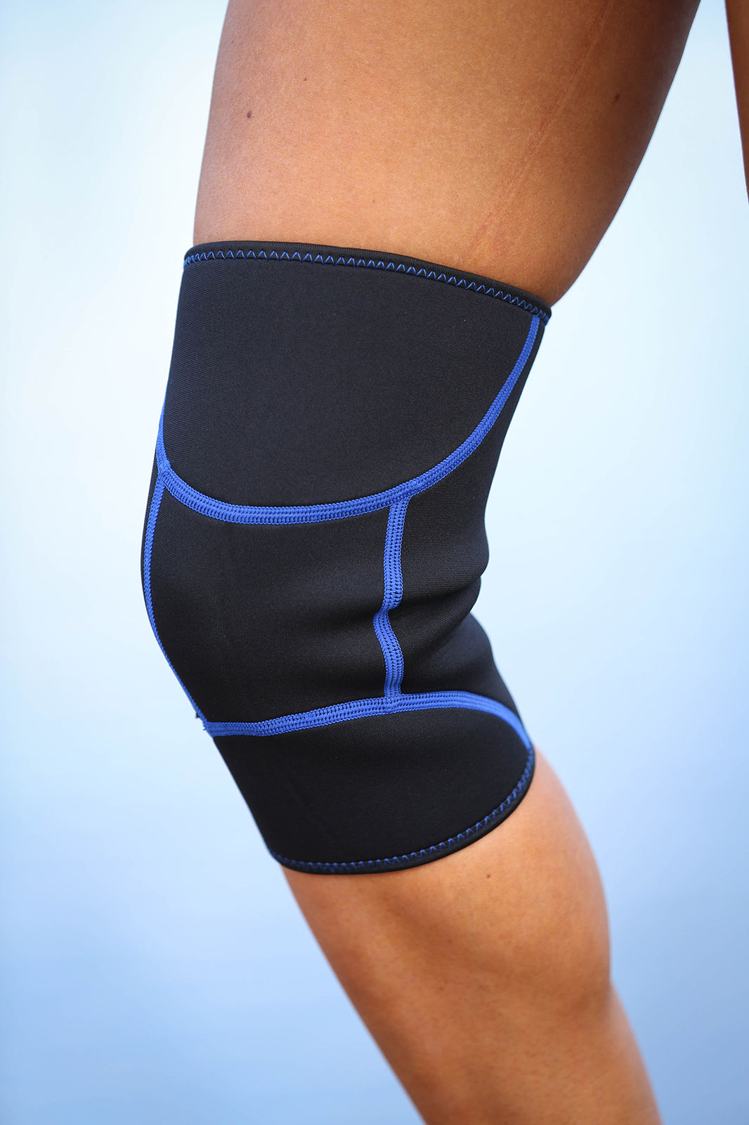 Black knee brace with blue accents on a person's knee against a light blue background