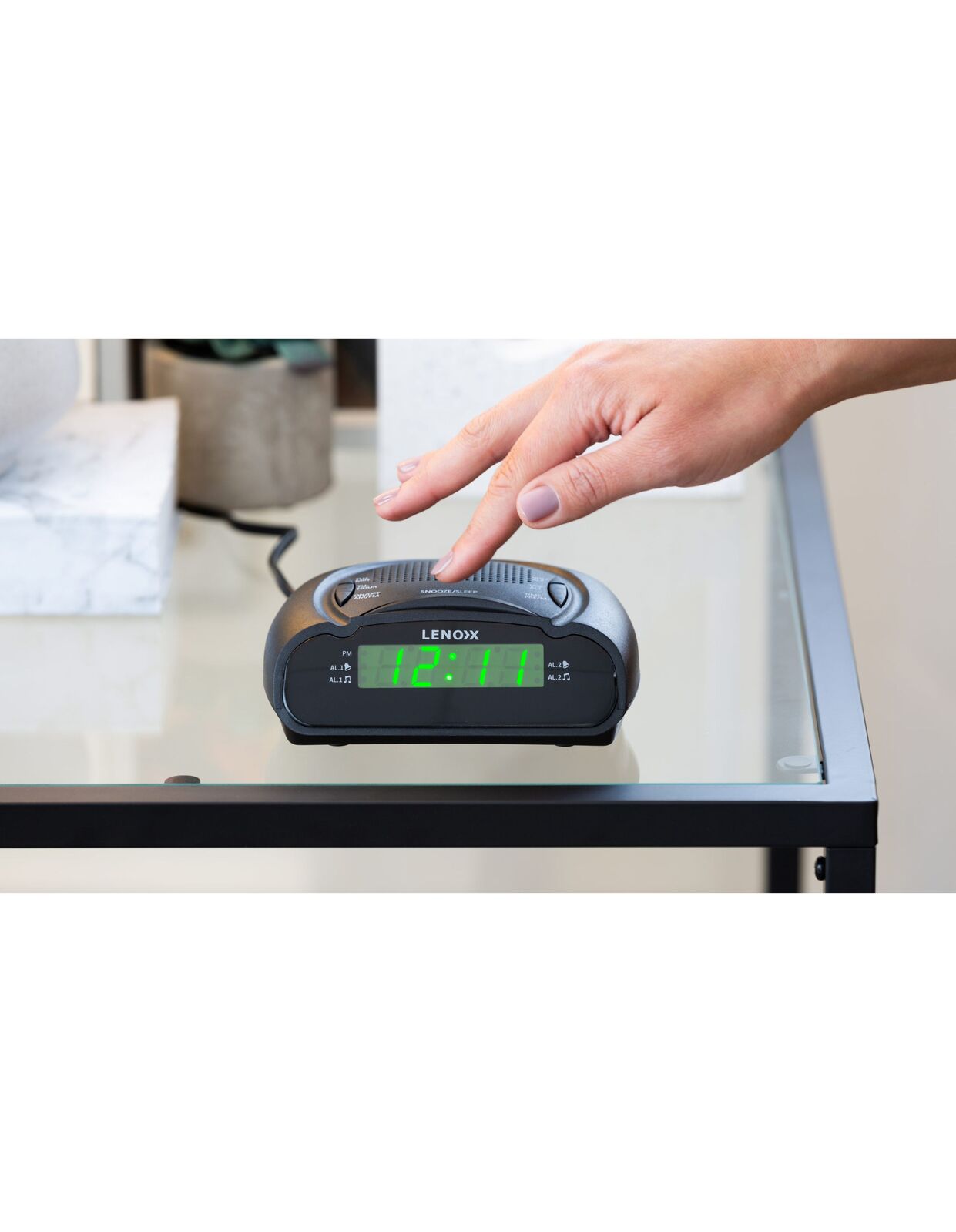 Lenox alarm clock on a glass surface with a hand reaching towards it
