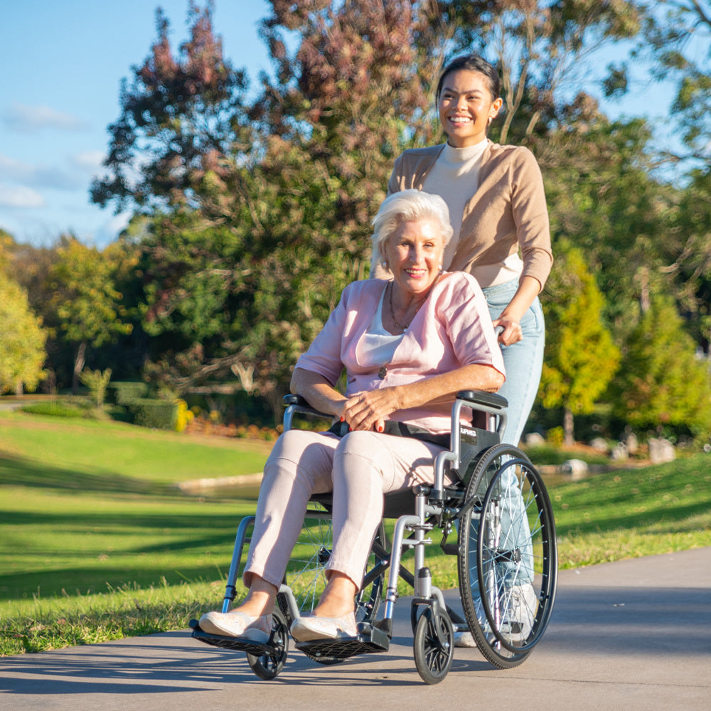 Woman pushing an elderly woman in a wheelchair through a park