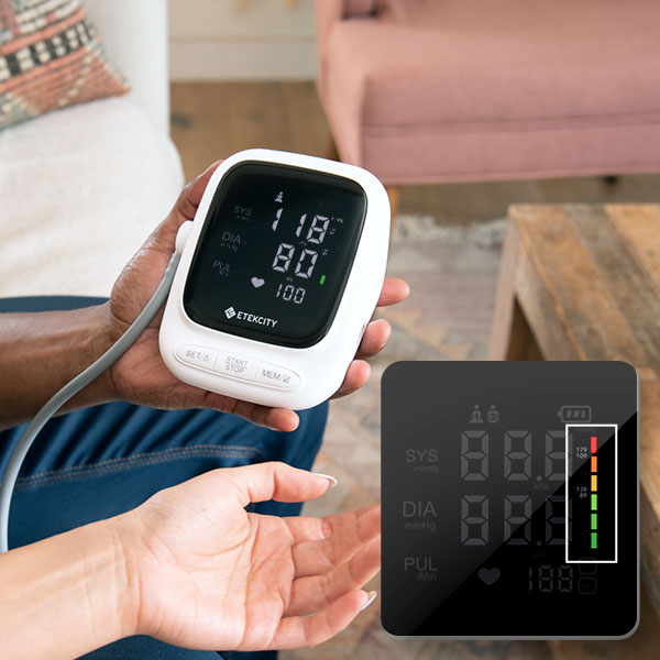 Hand holding a blood pressure monitor with a close-up inset showing the digital display.