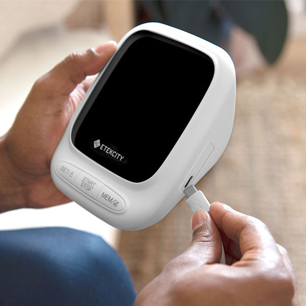 Person holding a white electronic device with a black screen, branded 'Etekcity', and plugging in a cable.