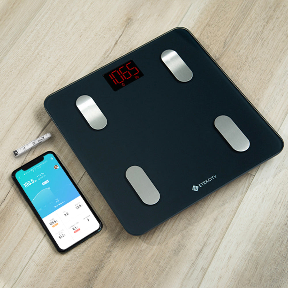 Digital bathroom scale on a wooden surface with a smartphone displaying app.
