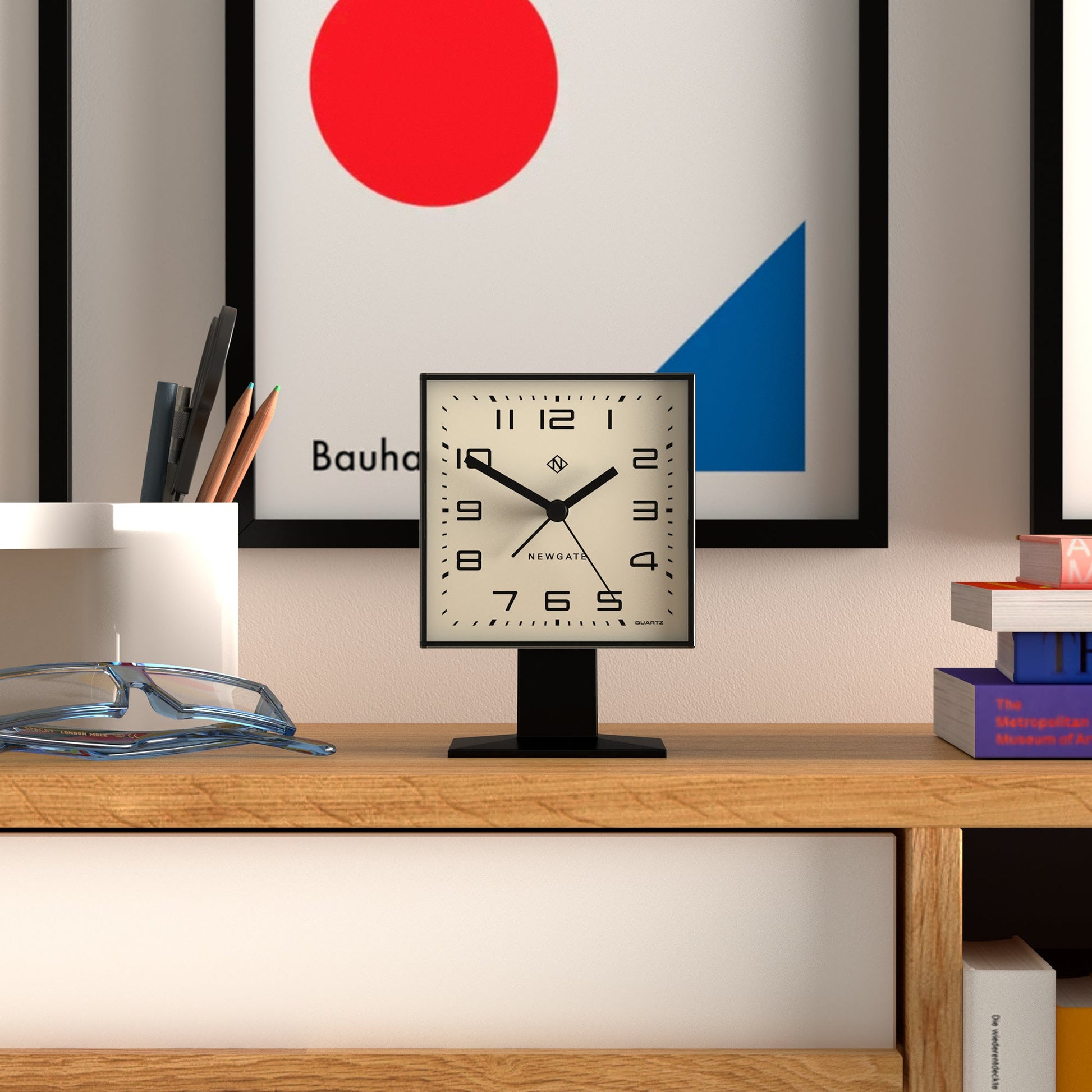 Desk with a clock, books, and a Bauhaus-style painting in the background