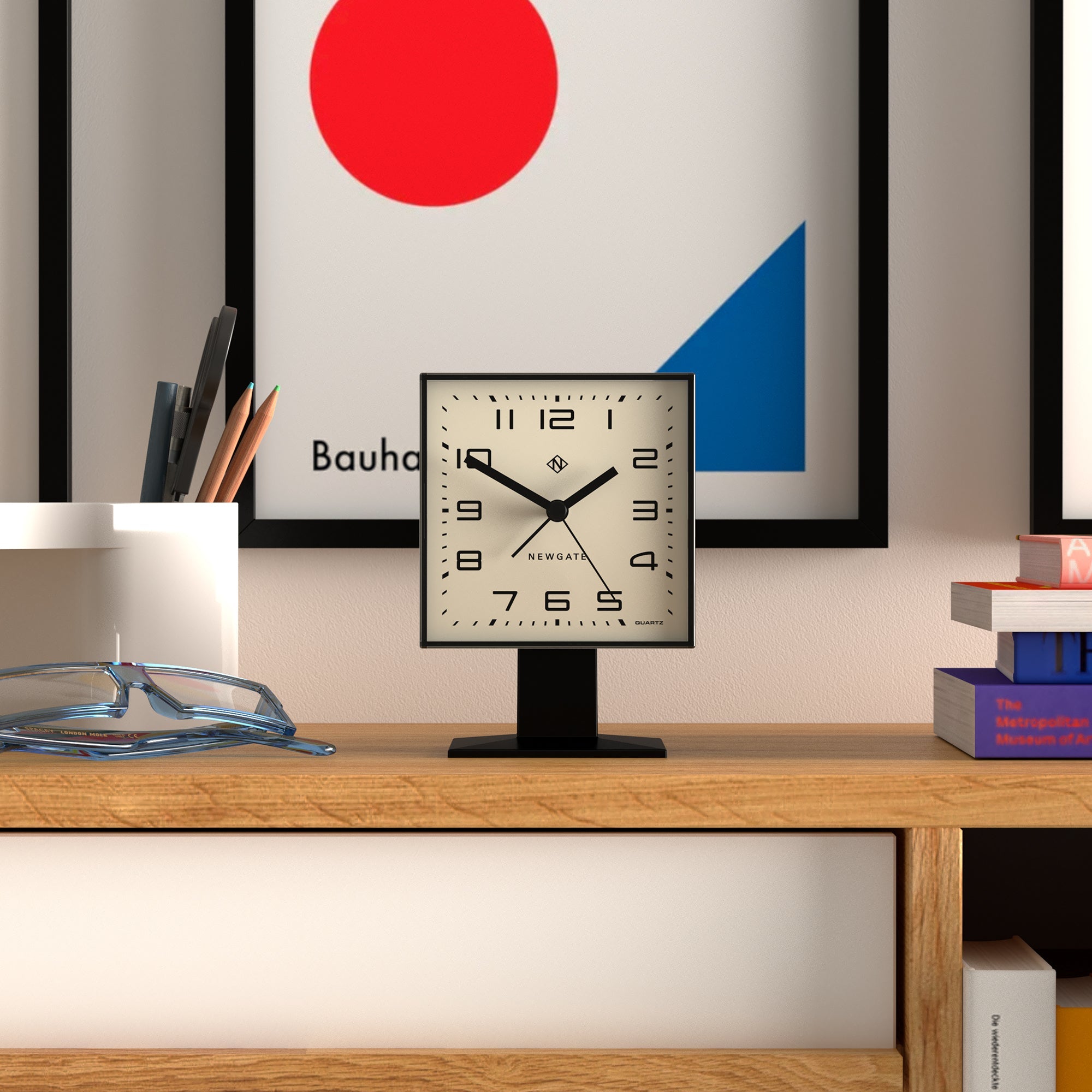 Desk with a clock, books, and a Bauhaus-style painting in the background