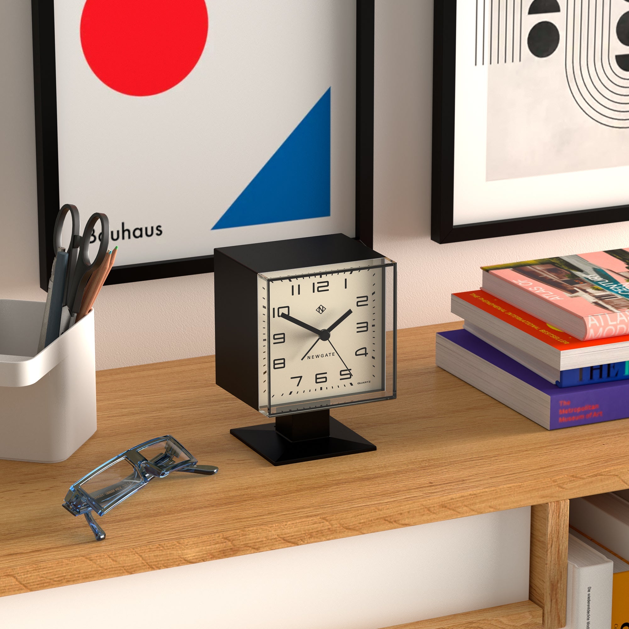 Desk with a clock, books, and office supplies against a wall with abstract art.