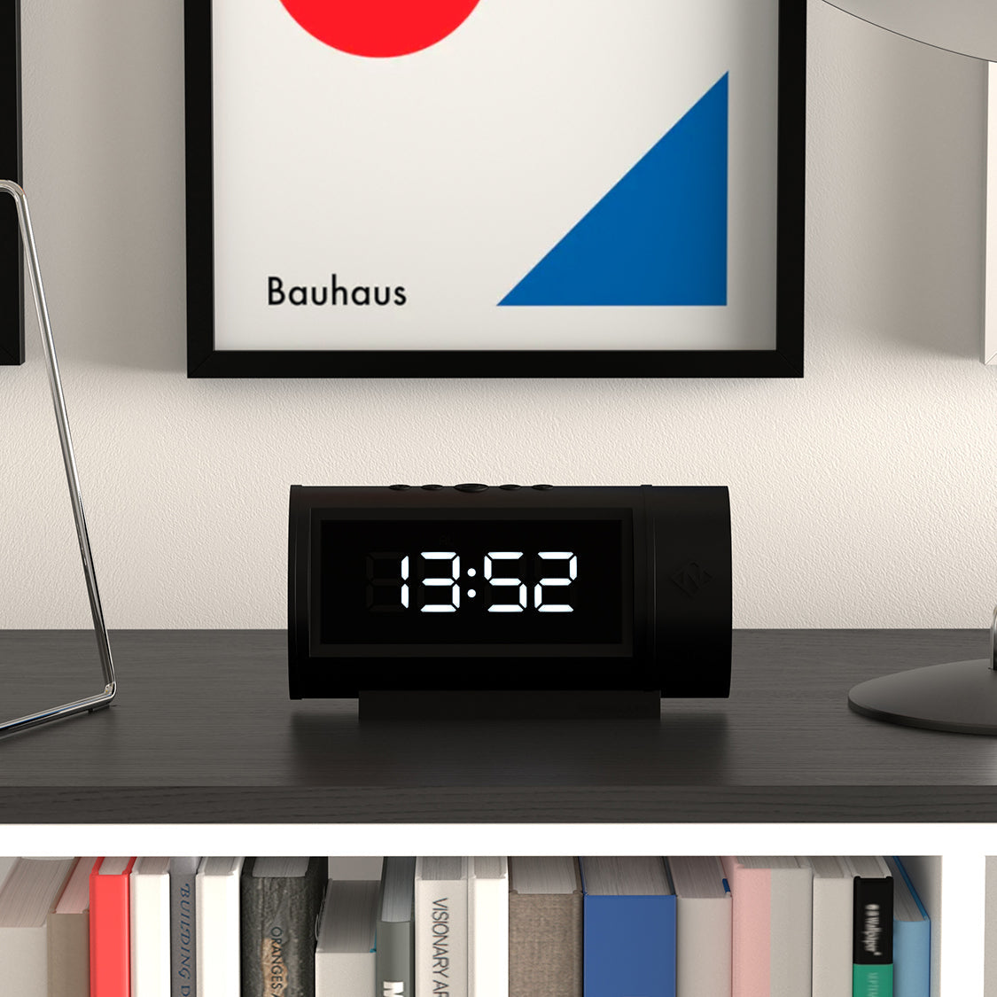 Black digital clock on a shelf with a Bauhaus art piece in the background