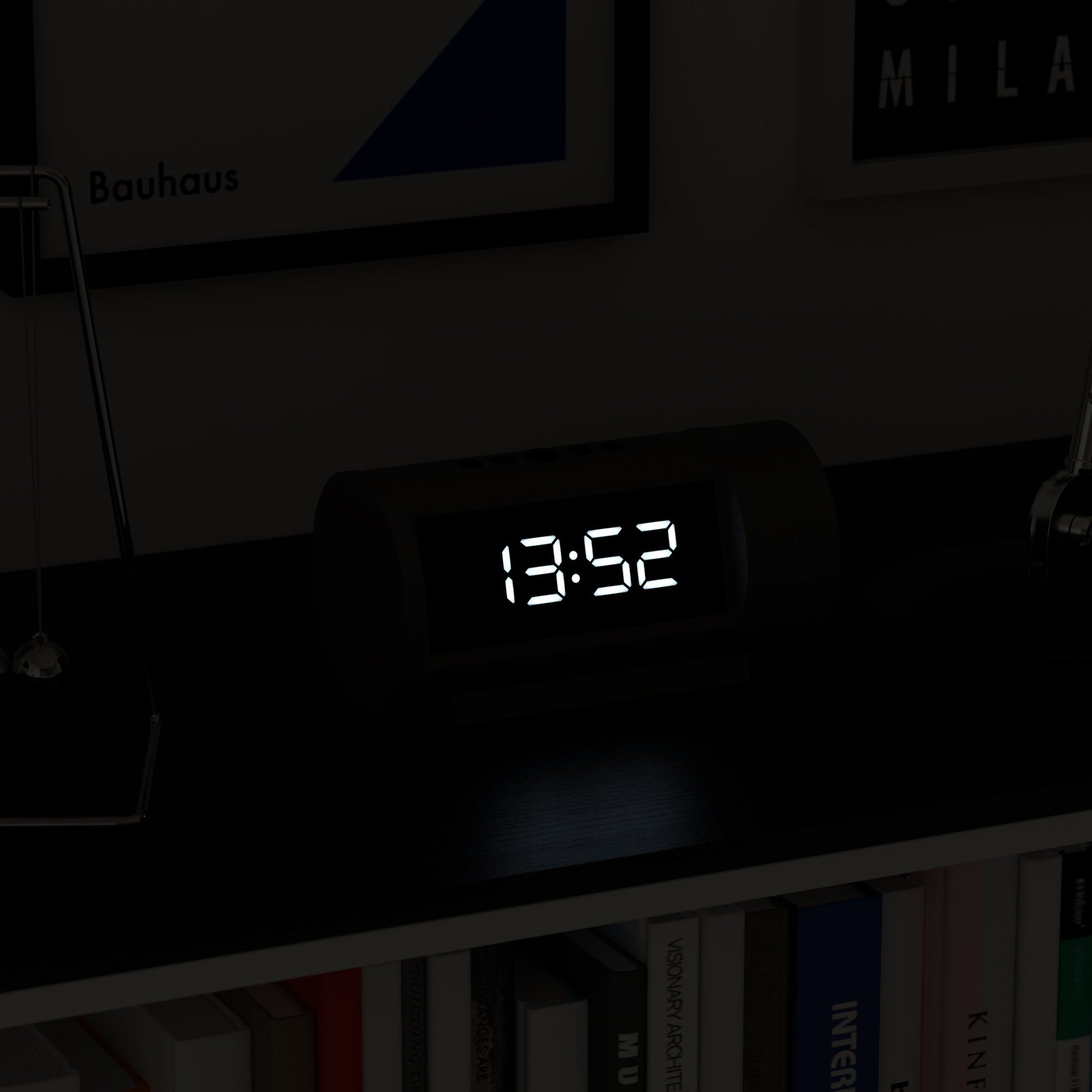 Digital clock displaying the time on a shelf with books and decorative items.