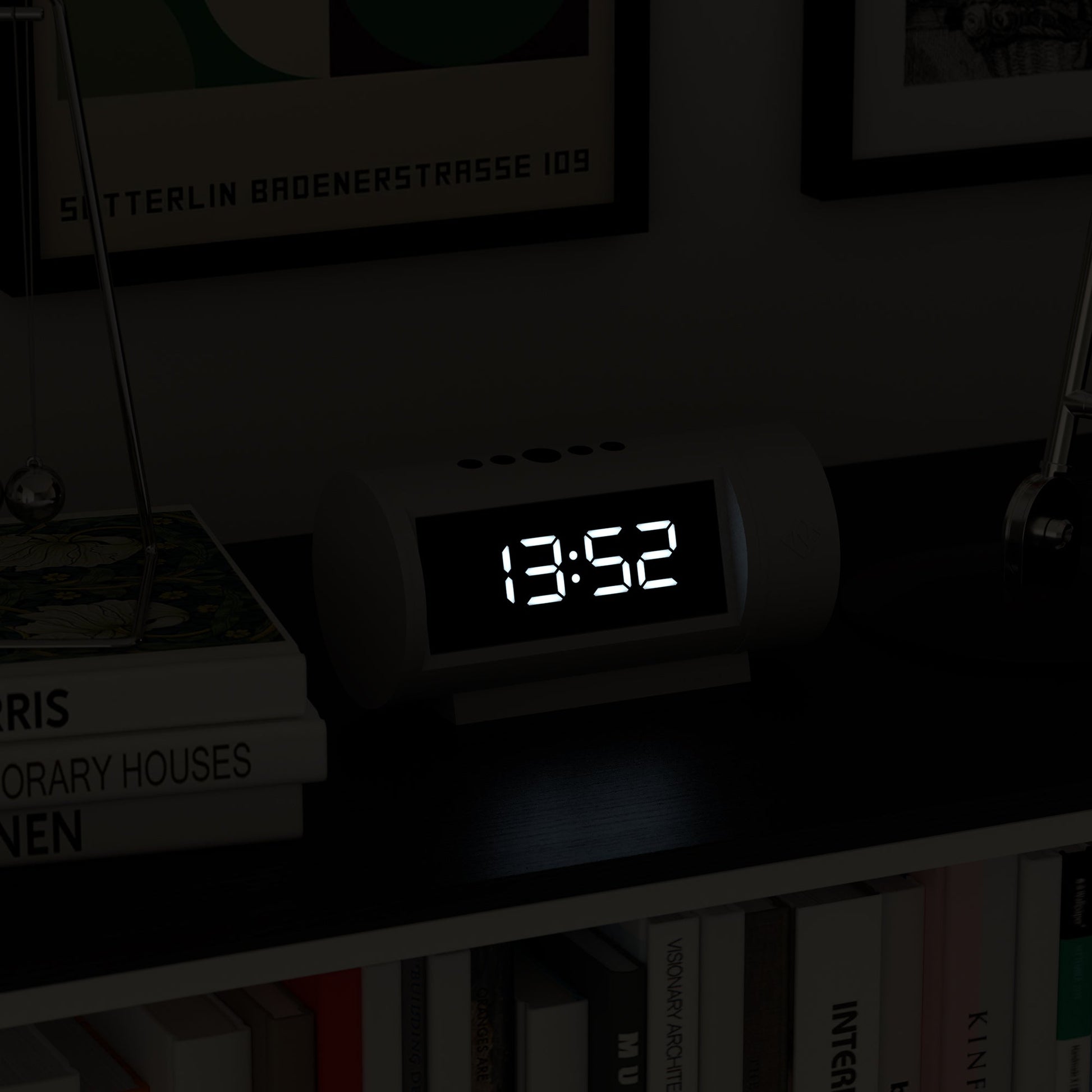 Digital clock displaying the time 13:52 on a shelf with books and decorative items.