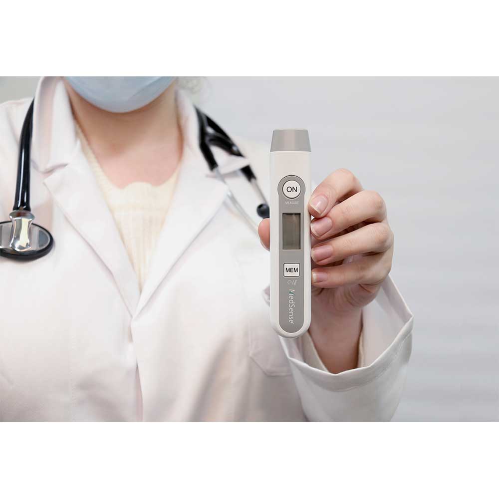 Person in a white coat holding a digital thermometer with a plain background