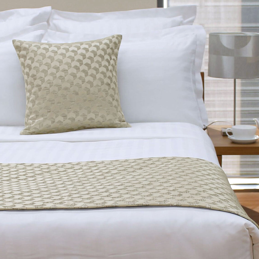 Bed with white bedding and a patterned beige pillow and throw blanket.