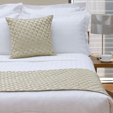 Bed with white bedding and a patterned beige pillow and throw blanket.