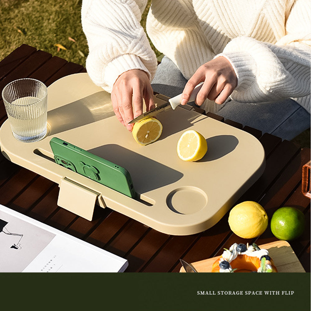 Person cutting lemons on a portable outdoor table with phone and glass.