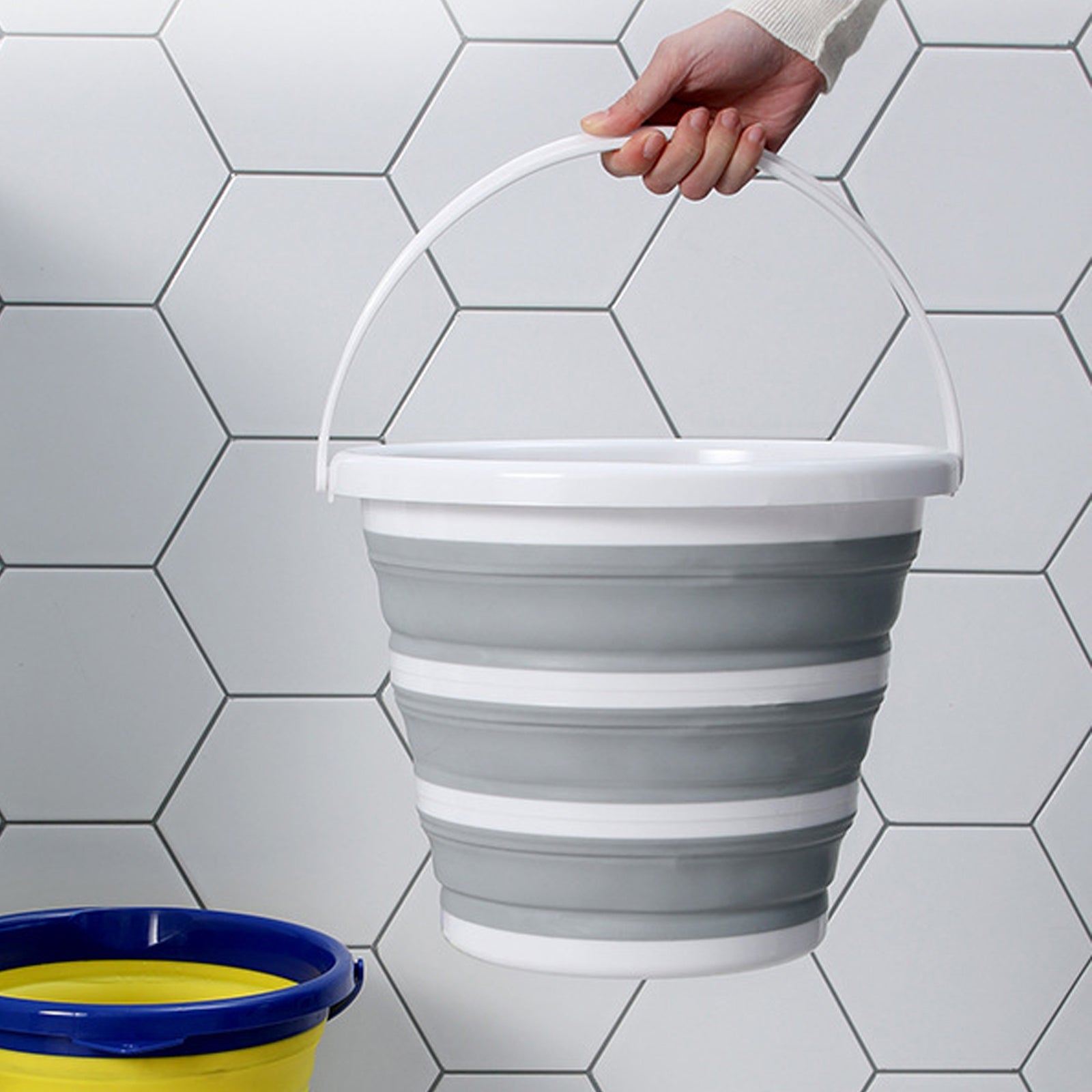 Collapsible gray bucket being held against a tiled wall.