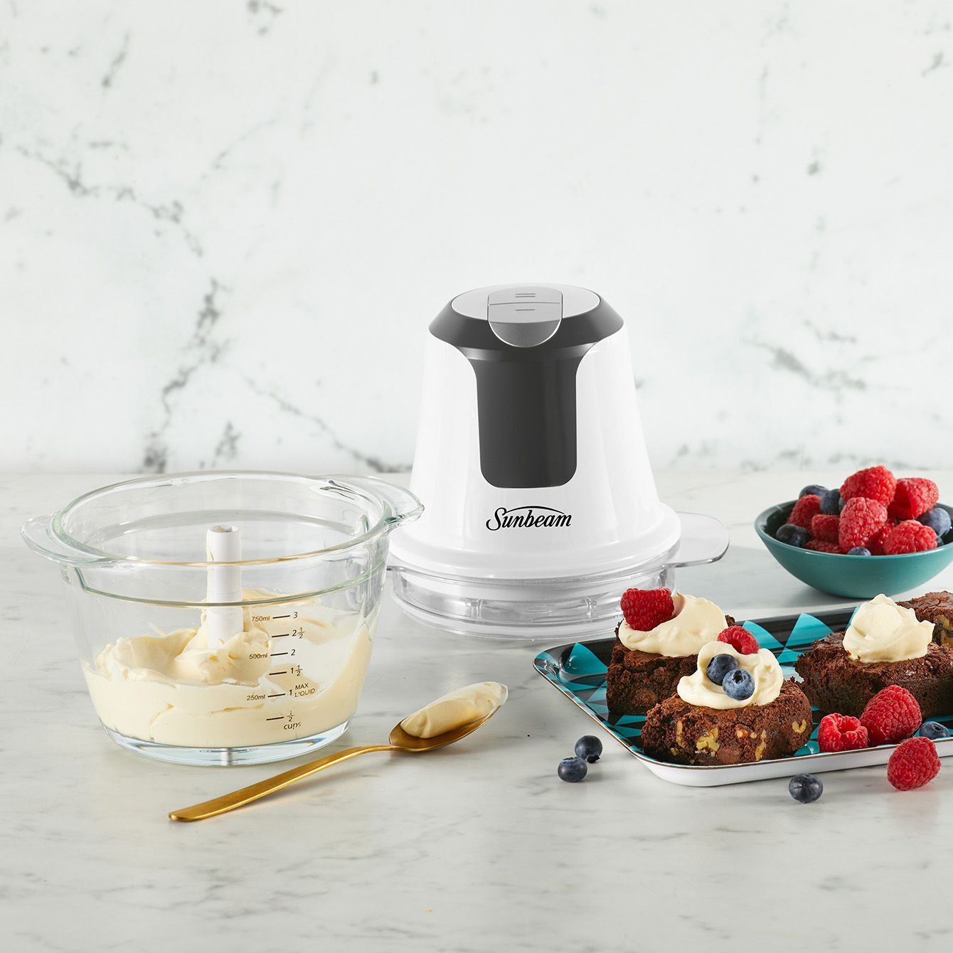 Sunbeam food processor on a marble countertop with desserts and ingredients