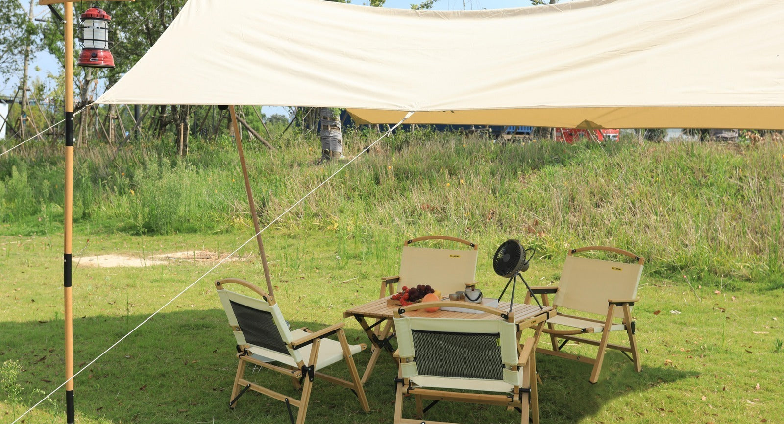 Camping setup with chairs, table, and tarp in a grassy outdoor area
