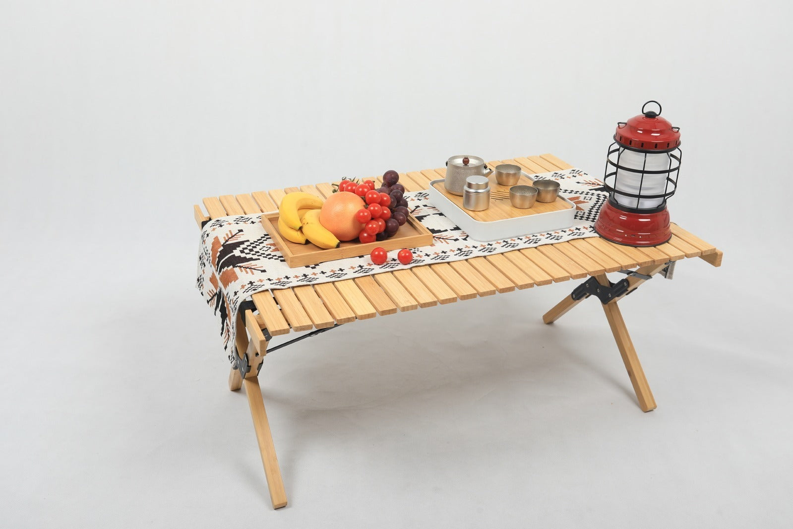 Wooden folding table with a tray of food and a lantern on a white background