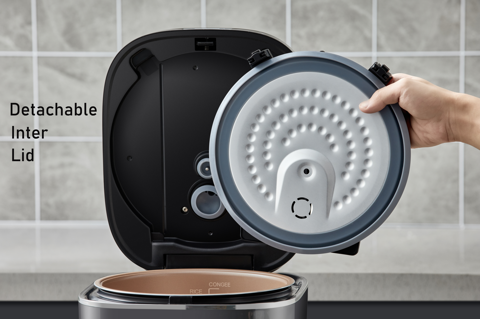 Hand holding a detachable inter lid of a kitchen appliance against a tiled wall background.