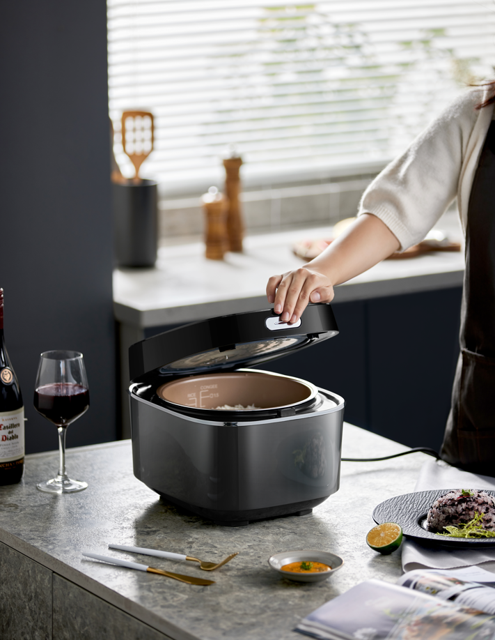 Person using a rice cooker on a kitchen counter with a glass of wine and food items around.