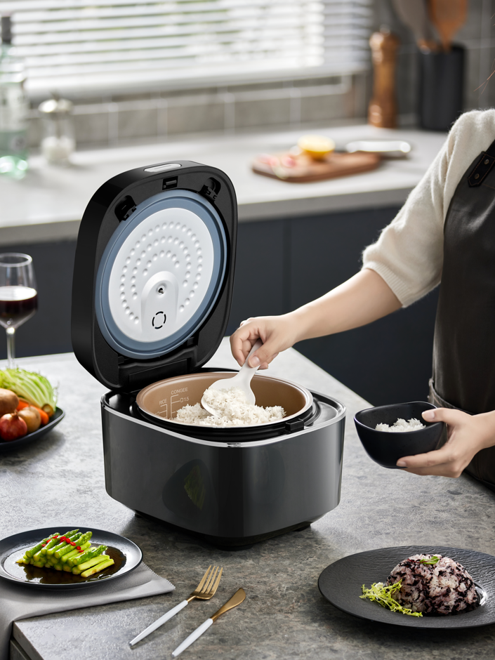 Person using a rice cooker in a kitchen setting with plates of food around.
