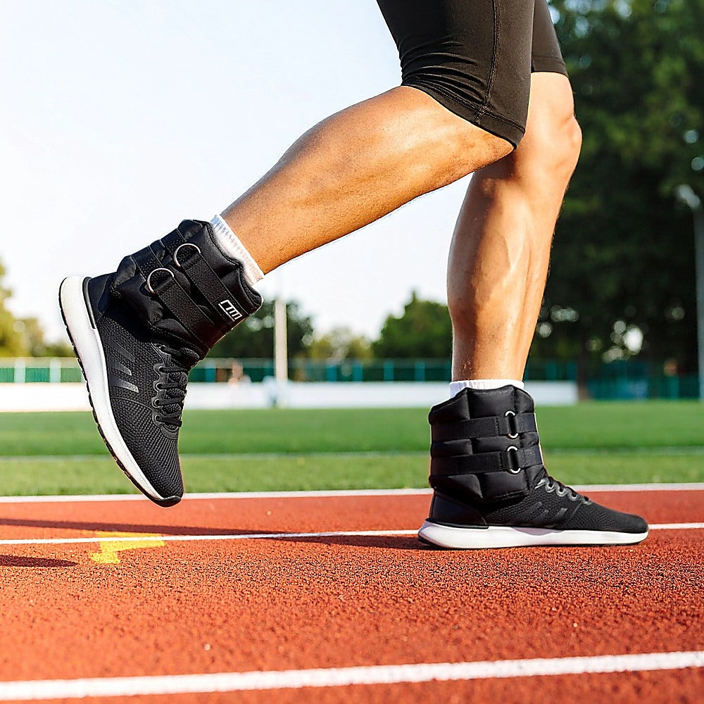 Person wearing black athletic shoes with white soles on a running track.