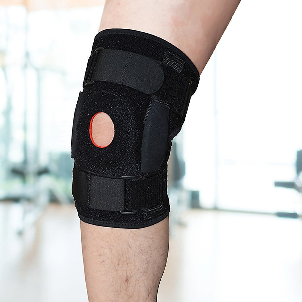 Black knee brace on a person's knee with a blurred indoor background
