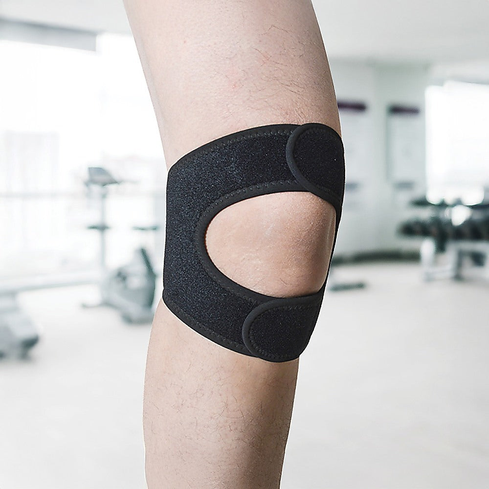 Black knee brace on a person's knee with a blurred indoor background