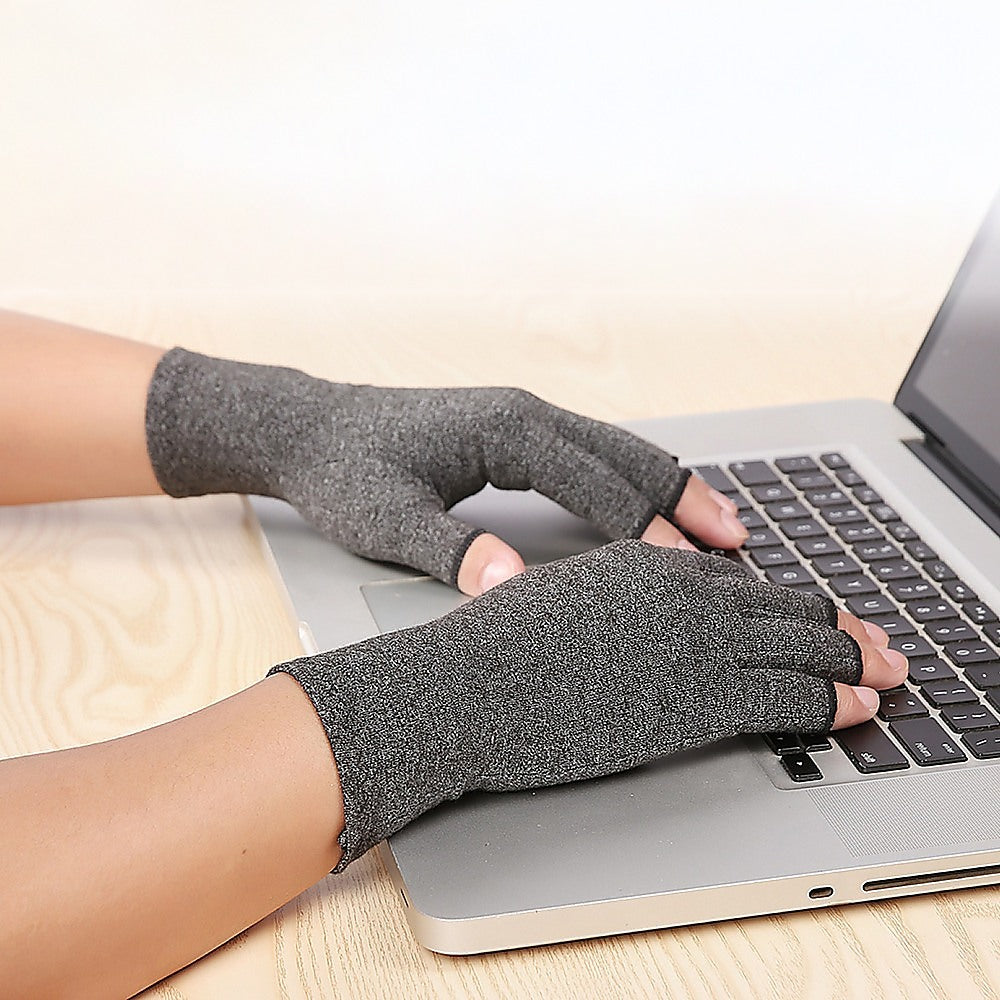 Person wearing gray compression gloves using a laptop on a wooden desk.