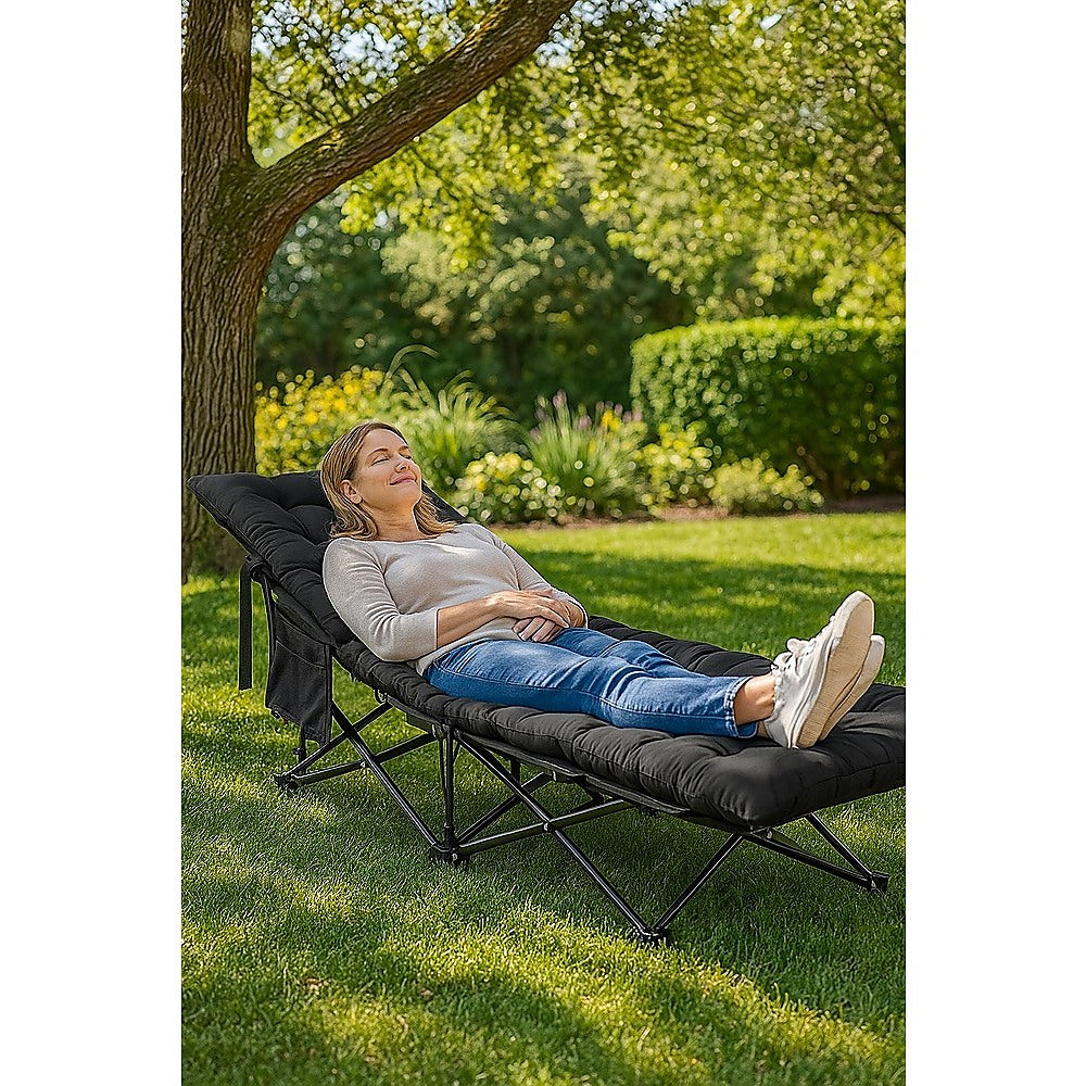 Woman relaxing on a black outdoor lounge chair in a garden setting.