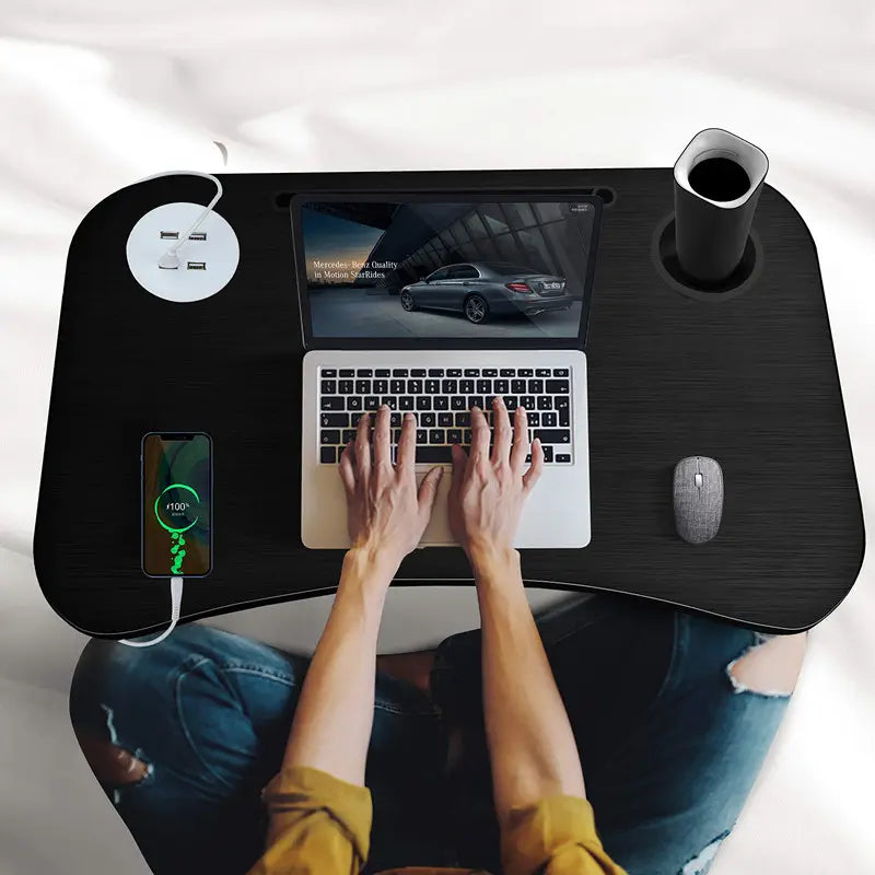 Person using a laptop on a black desk with a cup and phone.