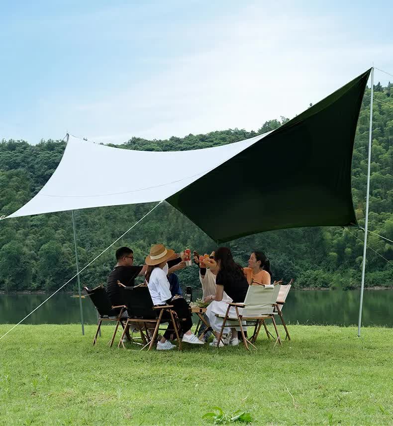 Group of people sitting under a large green and white canopy by a lake.