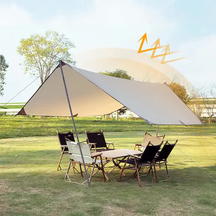 Outdoor setting with a large beige tent and chairs on a grassy field.