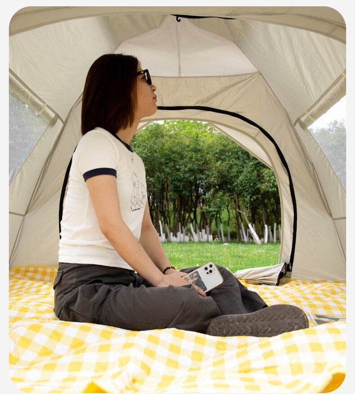 Person sitting inside a tent with a yellow checkered blanket, looking out at trees.
