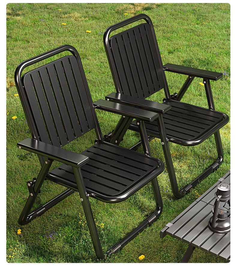Two black folding chairs on a grassy area with a small table and lantern in the background.