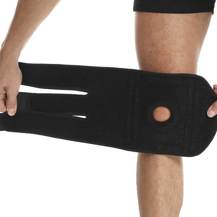 Black knee brace being worn on a person's knee against a white background