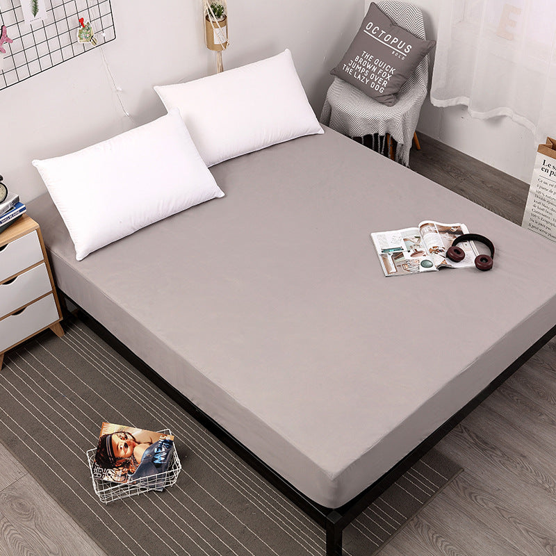 Gray fitted sheet on a bed with pillows and a small table in a bedroom setting.