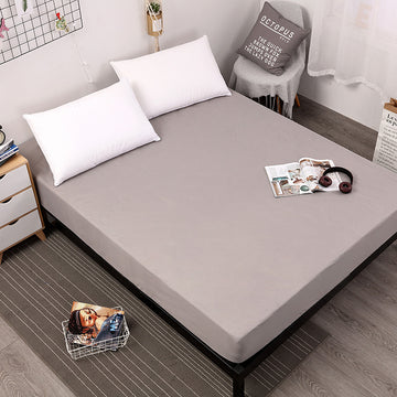Gray fitted sheet on a bed with pillows and a small table in a bedroom setting.