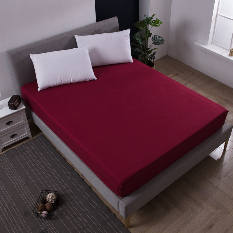 Red fitted sheet on a bed in a bedroom setting with pillows and a nightstand.